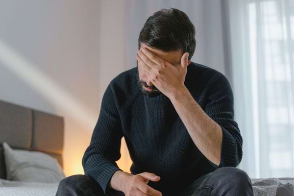 Un homme seul sur un lit cache son visage avec sa main.