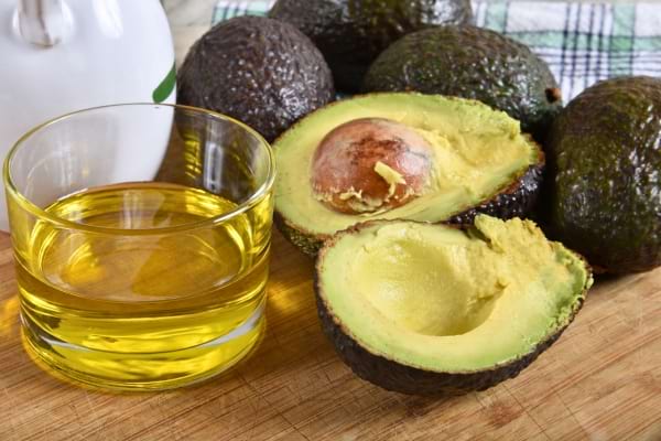 Avocats mûrs sur une planche avec un verre d’huile extraite à côté.