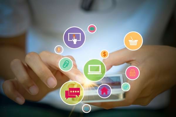 Une main utilise un smartphone entouré d’icônes d’applications colorées.