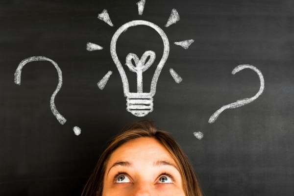 Jeune femme face à un tableau avec une ampoule dessinée au-dessus de sa tête, symbolisant une idée.
