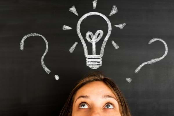 Femme regardant une ampoule dessinée sur tableau noir.