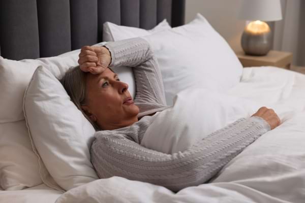 Une femme âgée allongée regarde le plafond, l’air anxieuse et incapable de dormir.