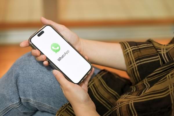 Une personne tient un téléphone avec l’écran de démarrage WhatsApp.