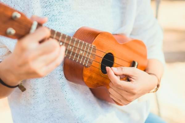 Une personne joue du ukulélé en extérieur, en pleine lumière du jour. 