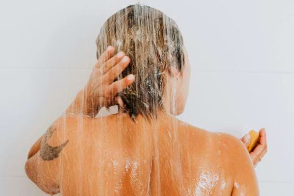 Une femme rince ses cheveux sous la douche avec du shampoing.