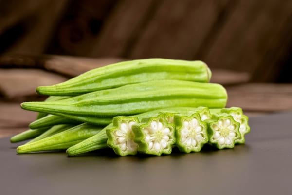 Gombos frais entiers et tranchés, posés sur une surface noire.