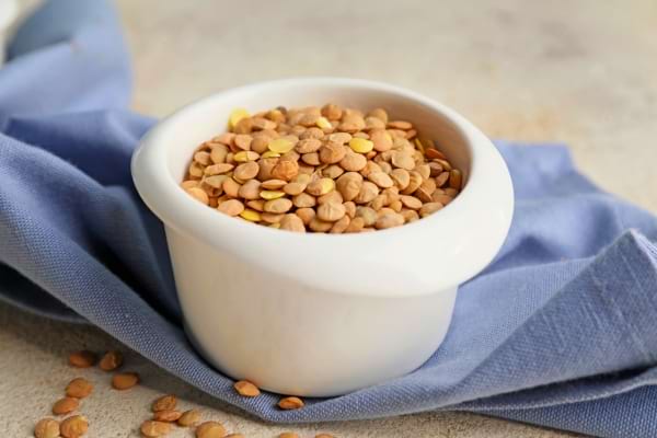 Lentilles blondes et corail dans un bol blanc sur un torchon bleu.