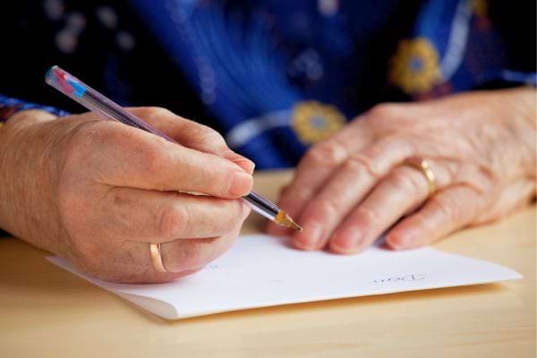 Une personne âgée écrit une lettre à la main.
