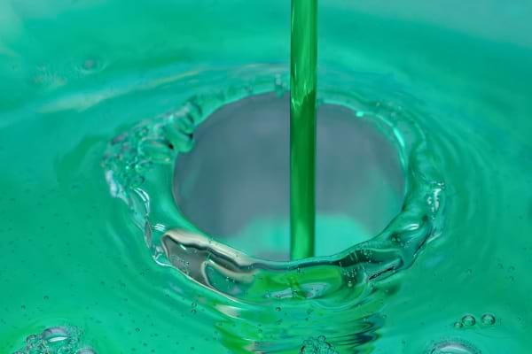 Un liquide vert coule dans un évier, formant des bulles autour de la bonde.