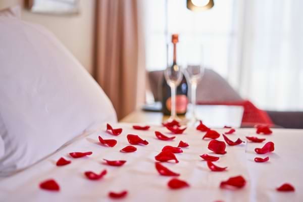 Des pétales de rose et une bouteille de vin sur un lit blanc.