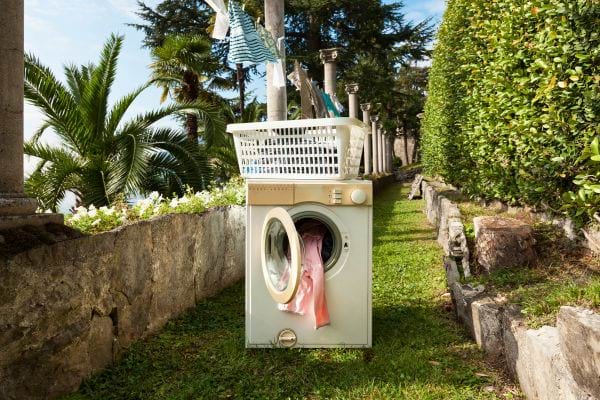 Une machine à laver placée dans un jardin avec du linge coloré.