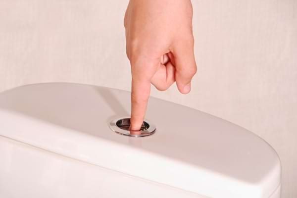 Une main appuie sur un bouton de chasse d'eau classique.