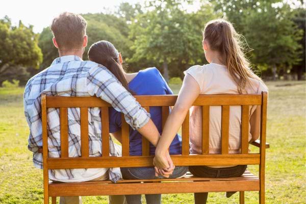 Sur un banc, un homme tient la main d&rsquo;une autre en cachette.