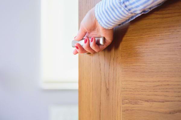 Femme en chemise bleue ouvre une porte en bois.
