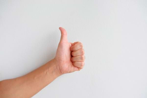 Main montrant un pouce levé devant un mur blanc.