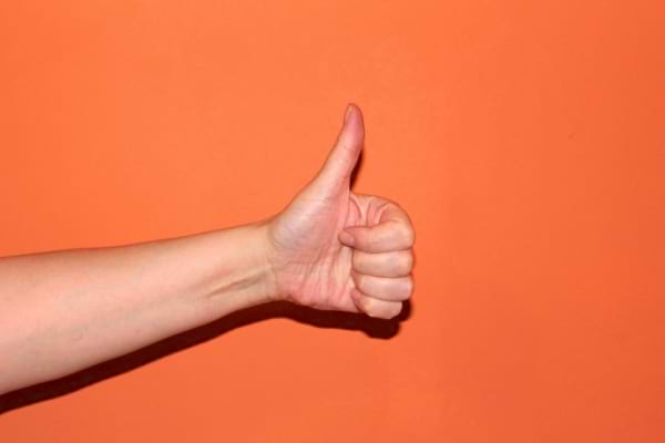 Main tendue avec le pouce levé sur fond orange, symbole d'accord ou de satisfaction.