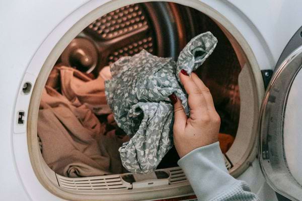 Une main retire un vêtement de la machine après lavage.
