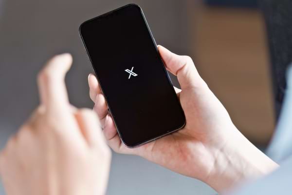 Une main tient un téléphone affichant le logo de l'application X (ex-Twitter).