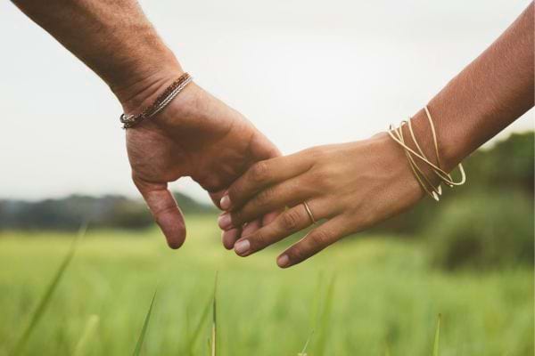 Un couple se tient tendrement la main dans un champ.