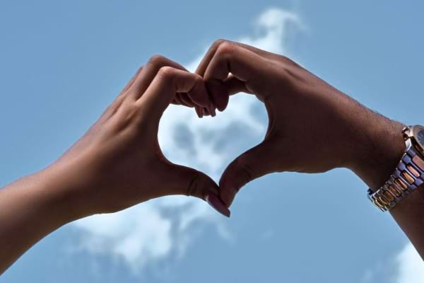Deux mains forment un cœur parfait devant un ciel bleu parsemé de nuages.