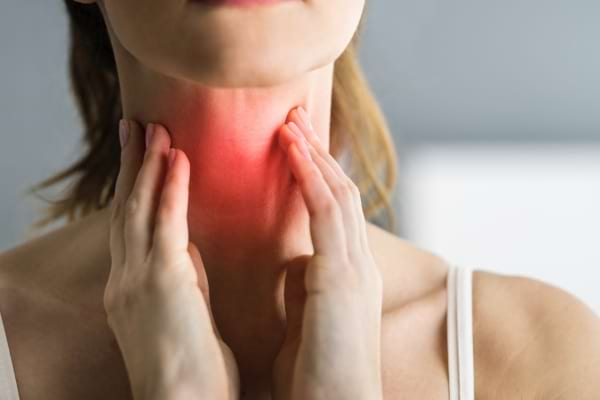 Une femme touche sa gorge enflammée, indiquant une douleur ou une gêne persistante au réveil.