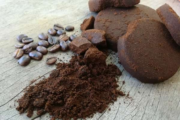 Marc de café frais et sec avec des grains de café sur une surface en bois brut.