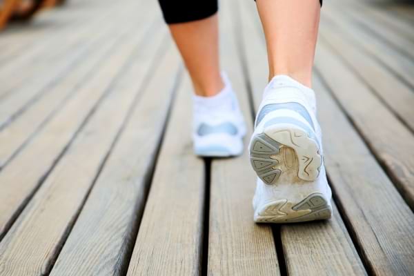 Personne qui marche sur un sol en bois avec des baskets blanches, vue de dos focalisée sur les pieds.