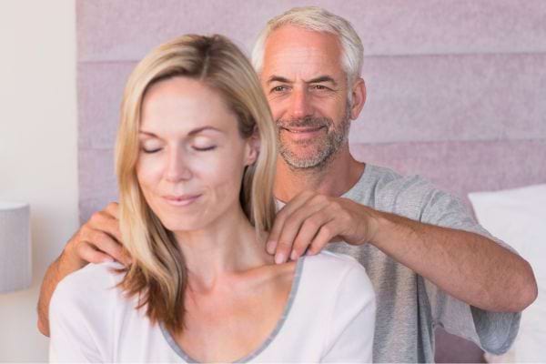 Un homme masse doucement les épaules de sa compagne.