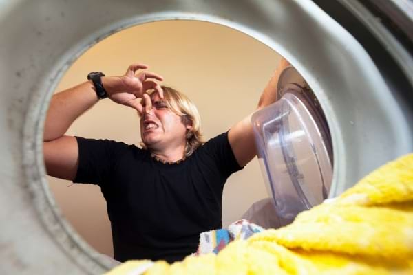 Homme tenant son nez face à une machine à laver à cause d’une forte mauvaise odeur.