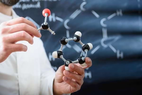 Un homme tient un modèle moléculaire en plastique devant un tableau de chimie.