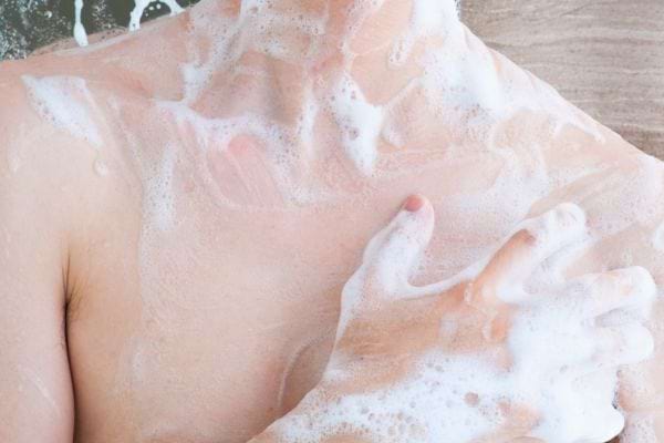 Une personne se lave le haut du corps avec une mousse abondante.