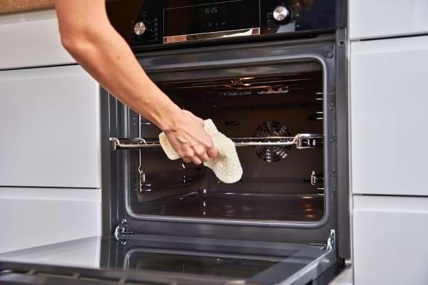 Main nettoyant l’intérieur d’un four ouvert avec un chiffon.