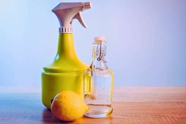 Un spray, une bouteille de vinaigre et un citron sur une table.