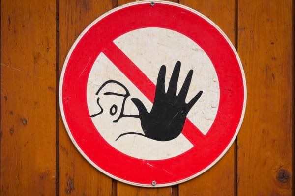 Un panneau d’interdiction avec une main noire stoppant un visage stylisé.