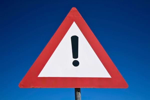 Un panneau de signalisation triangulaire rouge avec un point d'exclamation sur fond bleu ciel.