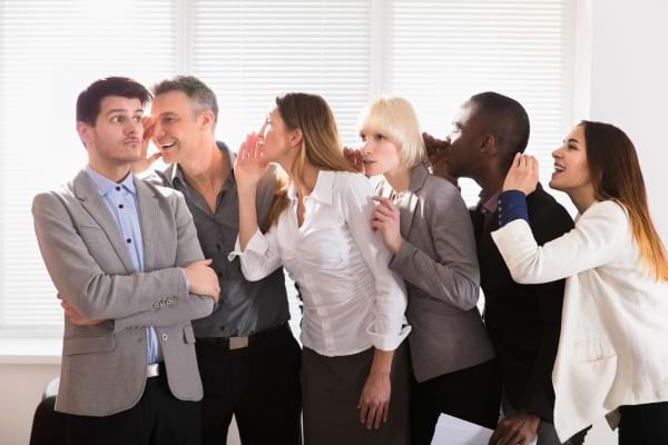 Des collègues chuchotent une rumeur en chaîne, le premier semble méfiant.