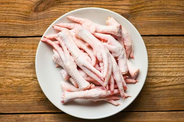 Une assiette blanche remplie de pieds de poulet crus posée sur une table en bois.