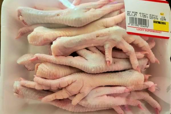 Des pieds de poulet crus emballés sous film plastique dans une barquette de supermarché.