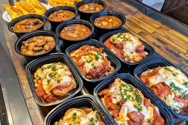 Plats préparés en barquettes avec accompagnements, exposés sur un comptoir.