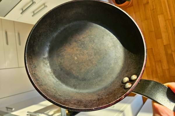 Poêle usée tenue en main, visible au-dessus du sol de la cuisine.