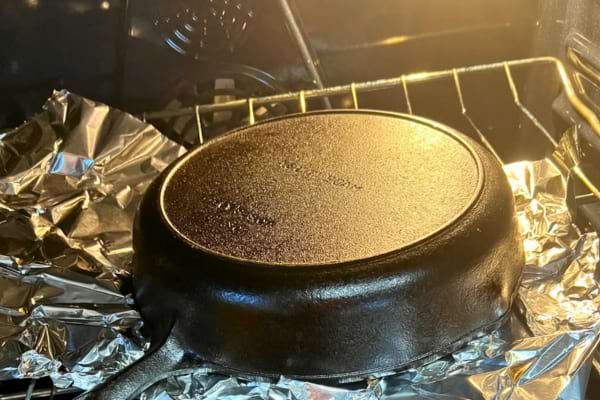 Poêle en fonte rangée à l’envers dans un four chaud sur papier alu.