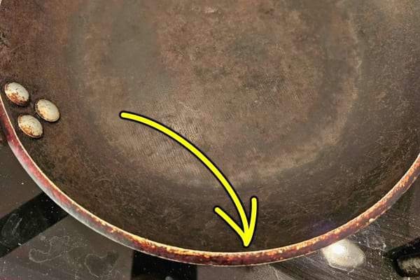 Vieille poêle avec flèche jaune montrant des traces de brûlures sur le bord.