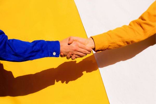 Deux personnes se serrent la main sur fond coloré.