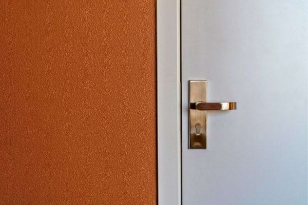 Porte fermée à poignée métallique sur mur orange.