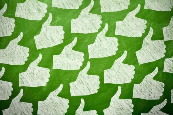 Motifs de pouces levés dessinés à la craie sur fond vert, exprimant l’approbation ou l’habitude courante.