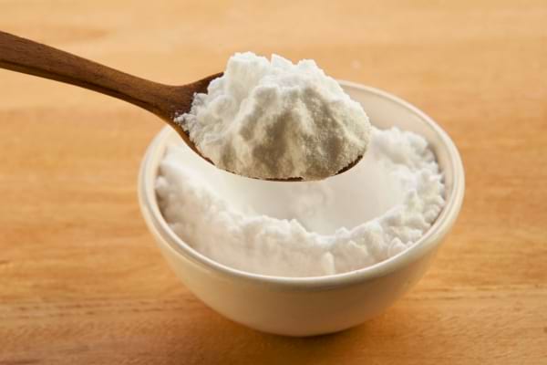 Une cuillère en bois remplit de bicarbonate au-dessus d’un bol blanc.
