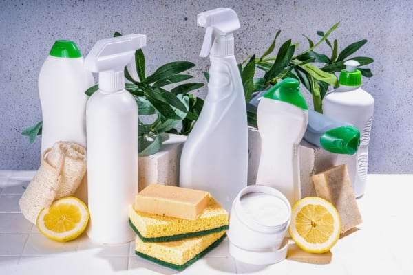 Produits ménagers naturels posés sur une table, accompagnés de citrons, éponges et savon pour un nettoyage écologique.