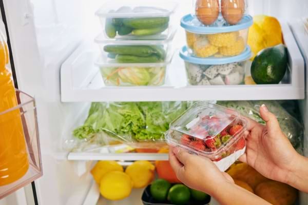 Une personne range une barquette de fraises dans un réfrigérateur bien organisé.