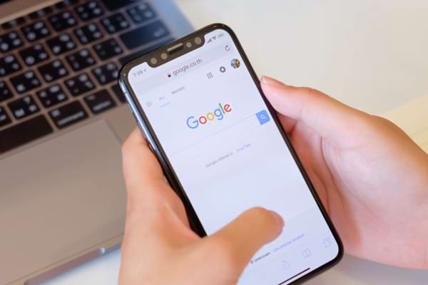 Une main tient un smartphone affichant Google devant un ordinateur portable.