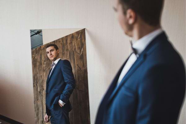 Un homme en costume se regarde avec assurance dans un miroir.